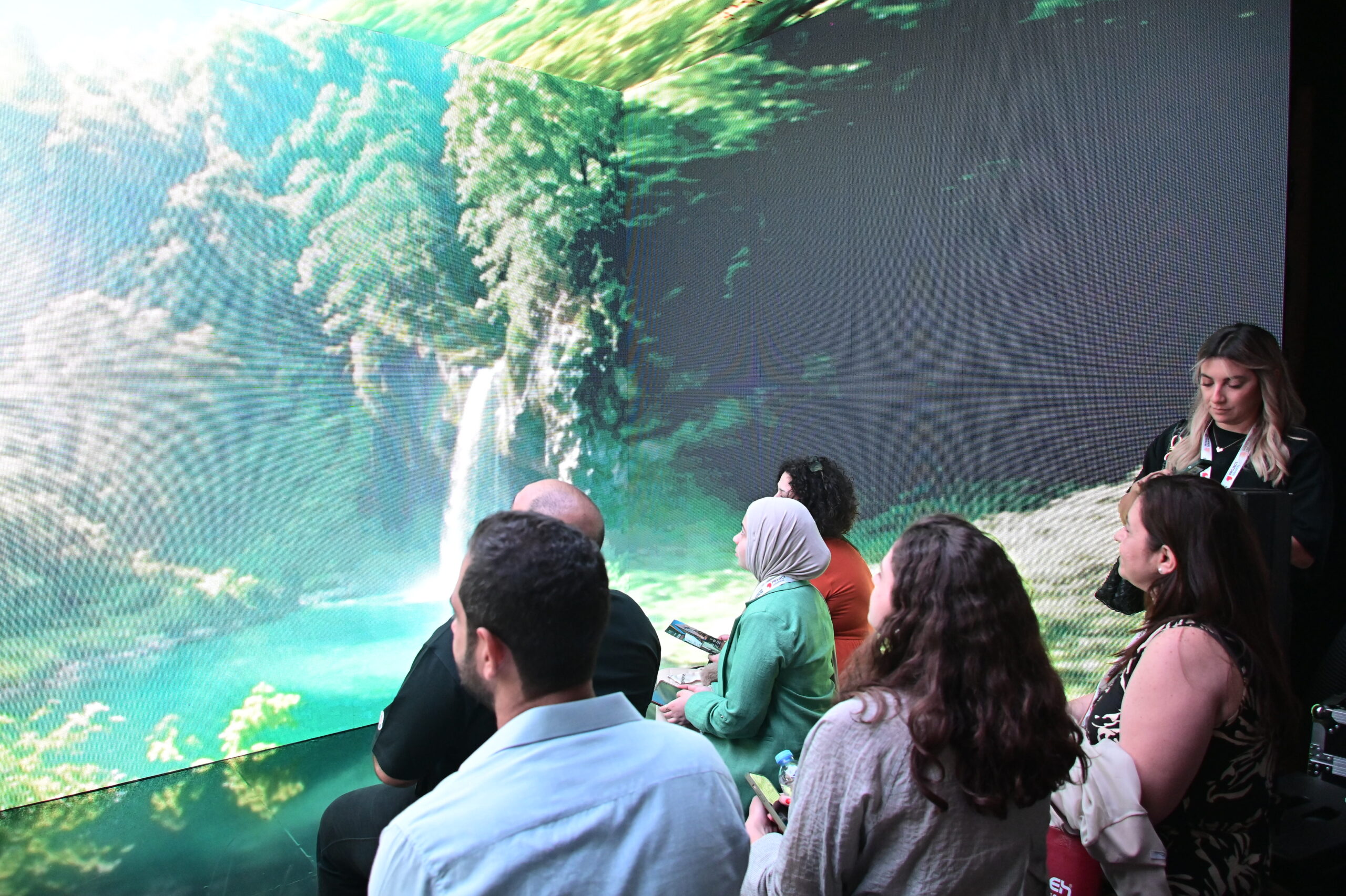 Visitors inside the immersive screen experience facing a waterfall